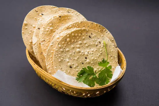 Udad papad in a cane basket with a coriander sprig